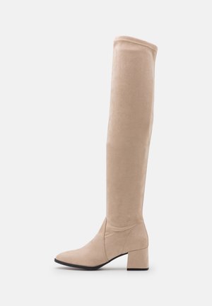 Botte haute beige en daim jusqu'au genou avec talon bloc bas et bout pointu, montrée de profil sur fond uni.
