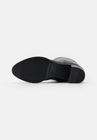 Spodní část černé kožené boty s hladkou texturou, gumovou podrážkou a zaoblenou špičkou. Jemný vzor podešve pro lepší přilnavost.