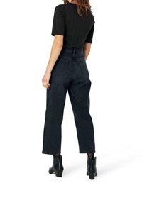 Korkeavyötäröiset mustat farkut suoralla leikkauksella, joissa on kaksi takataskua ja käännetyt lahkeet; yhdistetty tiukasti istuvaan mustaan teksturoituun toppiin.