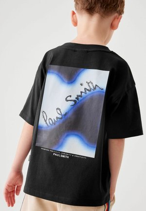 Musta puuvillapaita, jossa on suuri grafiikka sinisistä ja mustista aalloista sekä teksti "Paul Smith" käsinkirjoitetussa fontissa. Yksinkertainen pyöreä pääntie.