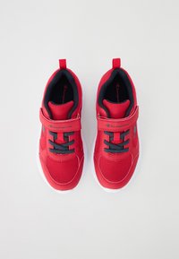 Pantofi sport roșii din plasă, cu un sistem de prindere Velcro, accente negre și talpă din cauciuc alb; au șireturi groase gri și un interior pădurit.