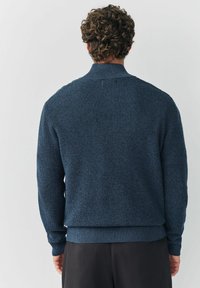 Tengerészkék kötött pulóver texturált mintával, bordás mandzsettákkal és aljjal. Álló gallérral és laza szabással készült.