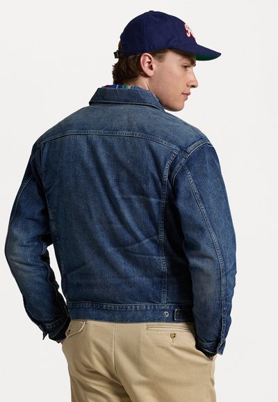 Mørkeblå denimjakke med klassisk passform, med krage, knappede mansjetter og detaljer på ryggen. Kombinert med lyse khaki-bukser.