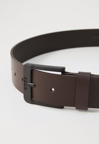Ceinture en cuir brun avec une finition lisse, dotée d'une boucle rectangulaire en métal noir et de trous renforcés pour l'ajustement.