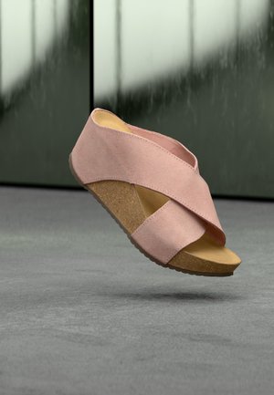 Sandale compensée en daim rose avec des brides croisées et une semelle en liège flottant au-dessus d'une surface grise sur un fond vert flou.