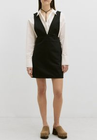 Zwarte denim jurk met een V-hals en brede schouderbanden, van textuurstof, gecombineerd met lichtbruine klompen met een blokhak.