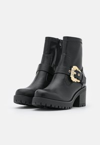Botas de tobillo de cuero negro con un tacón grueso, que cuentan con una decoración de hebilla dorada y cremallera lateral. Suela resistente para una mejor tracción.