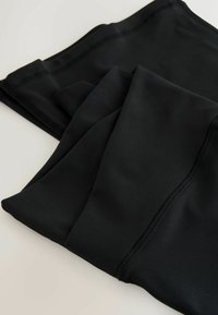 Černá, elastická látka s hladkým povrchem; skládací design ukazující viditelné švy a okraje, ideální pro sportovní nebo pohodlné oblečení.