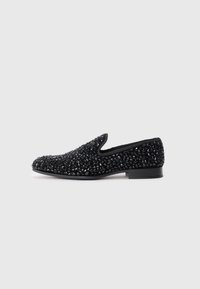 Black slip-on flat shoe covered in shiny black beads with a low heel, shown in profile on a white background.