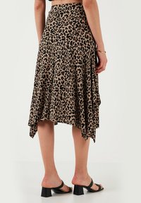 Leopardprint rok in bruin en zwart, met een high-low zoom, vloeiend materiaal en een zachte textuur. Gecombineerd met zwarte blokhak sandalen.