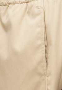 Κοντινή λήψη μπεζ βερμούδας με ελαστική μέση με σούρες και ορατή ραφή πλαϊνής τσέπης.
