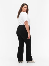 Black flared jeans with pockets, high waist design, and a smooth texture, paired with a white t-shirt and light footwear.