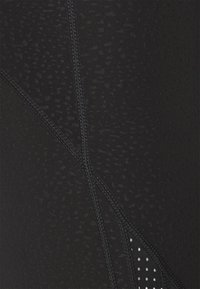 Leggings neri con una texture liscia, finitura opaca sottile, dettagli delle cuciture a contrasto e una sezione con piccole perforazioni bianche.