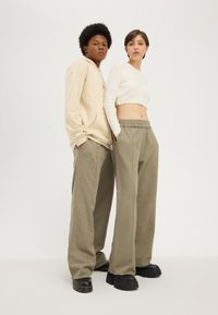 Beige hoodie with a kangaroo pocket, paired with a white cropped ribbed top. Loose olive-green pants with an elastic waistband and black platform shoes.