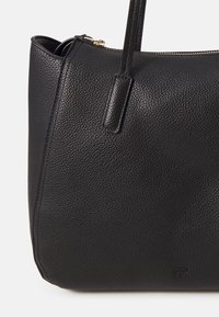 Sac cabas en cuir noir texturé avec deux poignées et une fermeture zippée sur le dessus, avec un petit logo embossé près du coin inférieur.
