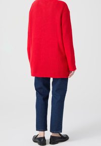 Red ribbed knit sweater with a loose fit, paired with dark blue straight-leg jeans and black loafers. Simple, casual outfit.