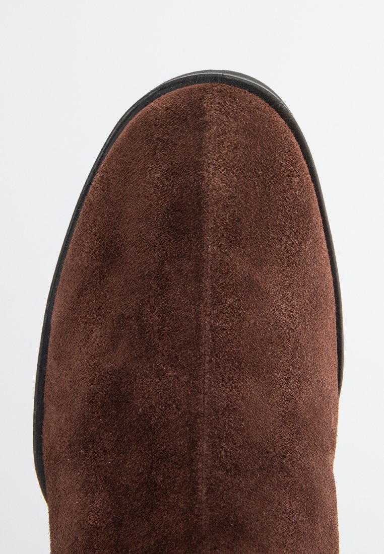 Brązowy zamszowy botek za kostkę o gładkiej strukturze, zaokrąglonym czubku i kontrastującej czarnej podeszwie. Charakteryzuje się czystym, minimalistycznym designem.