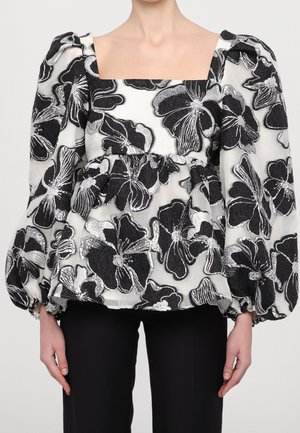 Blusa con estampado floral en blanco y negro, con mangas largas abullonadas y escote cuadrado, combinada con pantalones negros.