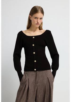 Schwarzer, gerippter Cardigan mit langen Ärmeln, quadratischem Ausschnitt und Details aus goldenen Knöpfen. Kombiniert mit hoch taillierten, gemusterten Hosen.