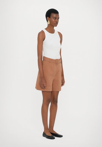 Shorts marron à ceinture avec une finition texturée, associés à un débardeur blanc ajusté et des chaussures plates noires. Boucles d'oreilles dorées en statement incluses.