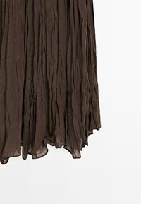 Brun plisseret stoffnederdel med lodrette folder og en let gennemsigtig tekstur, vist mod en hvid baggrund.