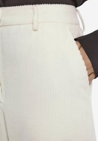 Weiße, gerippte Stoffhosen mit lockerer Passform, ausgestattet mit einem Kordelzugbund und Seitentaschen. Weicher Stoff mit dezenten Linienmustern.