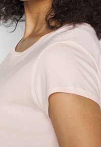 T-shirt a maniche corte rosa chiaro con scollatura rotonda e tessuto morbido. Presenta un sottile dettaglio di cucitura lungo le maniche e l'orlo.