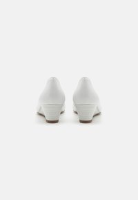 White wedge heels with a smooth leather exterior, rounded rear, and striped textured heel. Simple and elegant design.