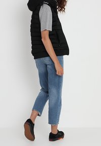 Black puffer vest with a hood over a gray short-sleeve shirt, paired with light blue cropped jeans and black sneakers with red accents.