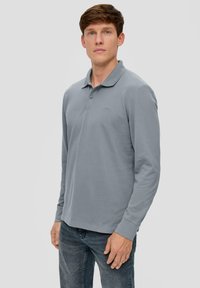 Langarm-Polohemd in Hellgrau, aus strukturiertem Stoff, mit einem Kragen und zwei Knöpfen, kombiniert mit dunklen Jeans.