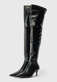 Svarte knelange støvler laget av blank lær, med spiss tå og smal hæl. Designet inkluderer et tilpasset skaft og synlige sømmer.