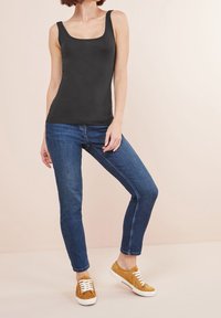Top nero senza maniche con scollatura quadrata, abbinato a jeans aderenti blu e sneaker color nocciola chiaro con lacci bianchi. Tessuto liscio.