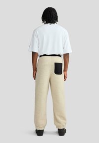 Beżowe dresy z polaru o teksturowanej powierzchni, z czarną kieszenią na prawej stronie i elastycznym pasem.