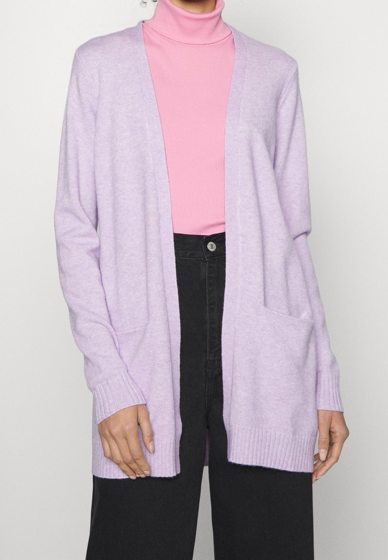 Ljuslila cardigan med öppen framsida, långa ärmar med ribbad manschett, som har två framfickor. Bärs över en rosa polotröja.