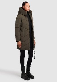 Pehmeda oliivroheline mantel, millel on kõrge krae, kammiliste mustritega ja lukuga. Kombineeritud mustade retuuside ja ankle-pikkuste mustade saapadega.