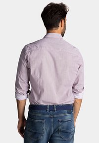 Heren overhemd in het roze met een patroon en opgerolde mouwen, voorzien van een klein geometrisch ontwerp. Geselecteerd met blauwe denim jeans en een bijpassende riem.