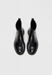 Bottes de cheville en cuir noir avec une finition brillante et des panneaux latéraux élastiques. Bout arrondi et semelle en caoutchouc contrastante. Design minimaliste.