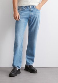 Svetlo modri ravni jeans s obrabljenim tekstilom, zasnovo s petimi žepi in kontrastnim šivanjem. Nosi se z debelimi črnimi loaferji.