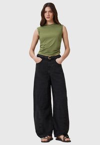 Olivgrön utanärmad topp, svarta vida byxor med texturerad yta, och svarta sandaler. Outfiten har ett vävt bälte med ett guldspänne.
