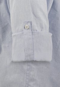 Lichtblauw langshirt manchet dat een knoopdetail en een gestructureerde stof toont. Kenmerkt zich door een strakke lijn en een gevouwen manchet voor een gestructureerde uitstraling.