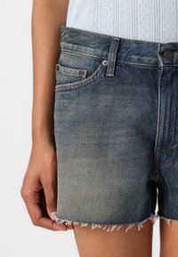Denim shorts in een vervaagde blauwe kleur, met een rafelige zoom, vijf zakken en metalen hardware-accenten. Textuur, casual pasvorm.