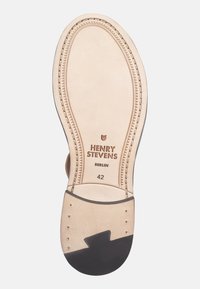 Suola di scarpa in pelle beige con un accento in gomma nera. Presenta un marchio e una taglia in rilievo, con bordo cucito e tacco arrotondato.