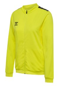 Helles gelbes Sportjacke aus strukturierter Baumwolle, mit durchgehendem Reißverschluss, hohem Kragen und schwarzen gemusterten Akzenten auf den Schultern.