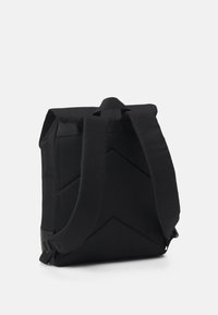 Sac à dos noir avec un design structuré, comportant un motif matelassé texturé, deux bretelles ajustables et une poignée supérieure pour le transport.