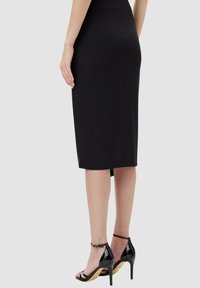 Gonna a tubino nera al ginocchio con design aderente e spacco sul retro, abbinata a sandali neri con tacchi alti e cinturini.