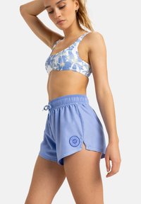 Blaue Sportshorts mit einem Kordelzugbund und seitlichen Schlitzen, kombiniert mit einem sportlichen BH im floralen Druck mit hellblauen und weißen Farben.