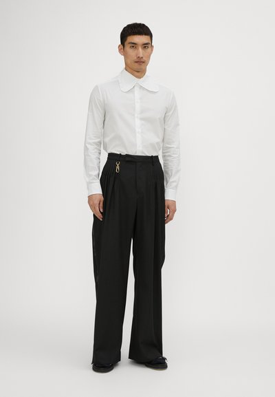 White long-sleeve shirt with a ruffled collar, paired with black wide-leg trousers featuring pleats and a gold hardware accent on the waist.