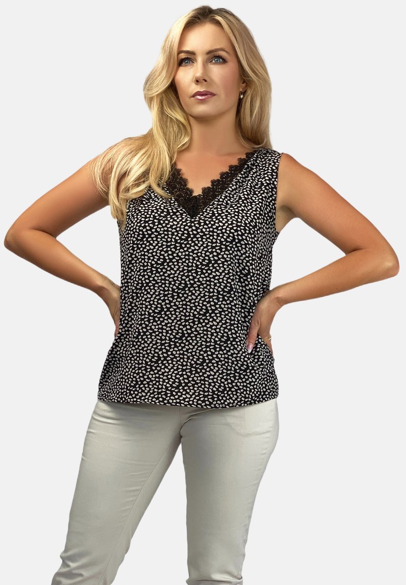 Czarny bezrękawnik w biały wzór kropek, koronkowe wykończenie przy dekolcie, zestawiony z jasnymi, dopasowanymi spodniami.