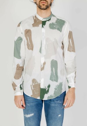 Camicia bianca con motivi a pennellate verdi e marroni. Presenta un colletto rialzato e maniche lunghe. Abbinata a jeans blu strappati.