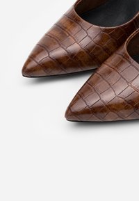 Scarpe in pelle marrone a punta con un motivo in croccodile, caratterizzate da una finitura liscia e lati aperti per la traspirabilità.